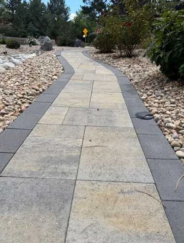 Rectangular paver walkway with dark borders surrounded by decorative river rock.