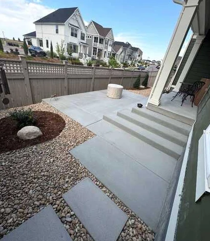 Concrete patio and broad steps adjoining a covered porch and river-rock planting beds.