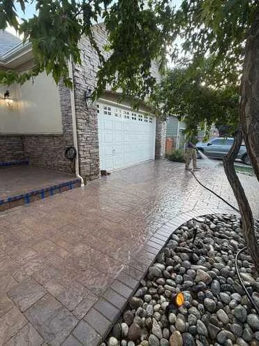 Curved decorative driveway framed by river-rock beds, trees and landscape lighting.