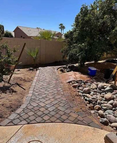 Curved multicolor paver walkway with a contrasting border beside decorative river rock.