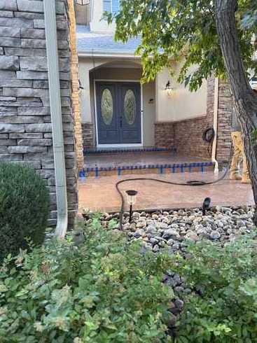 Front entry and porch with decorative paving, planting beds and stone accents.