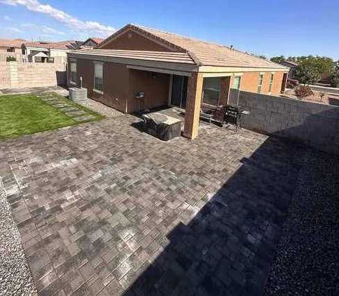 Broad gray paver patio extending from a covered porch with adjacent lawn.