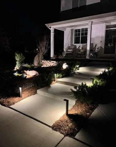 Concrete entry walkway and steps illuminated by warm low landscape lights at night.