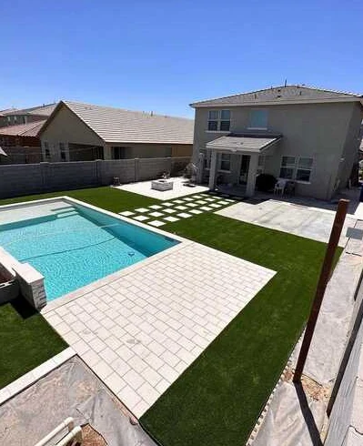 Poolside paver terrace and turf lawn with geometric stepping stones beside the home.